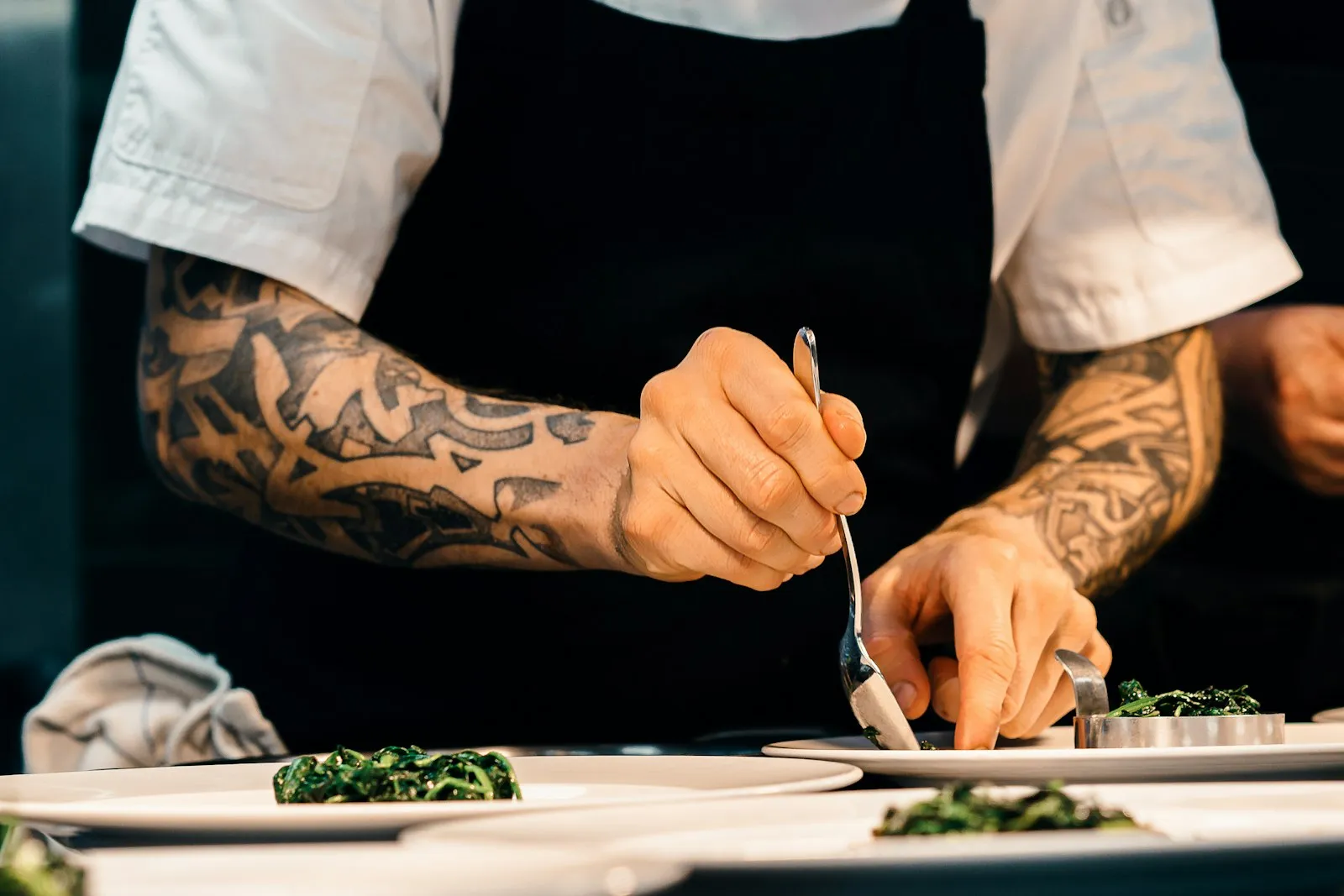 A chef at work in a domestic kitchen, plating a dish under warm side light.