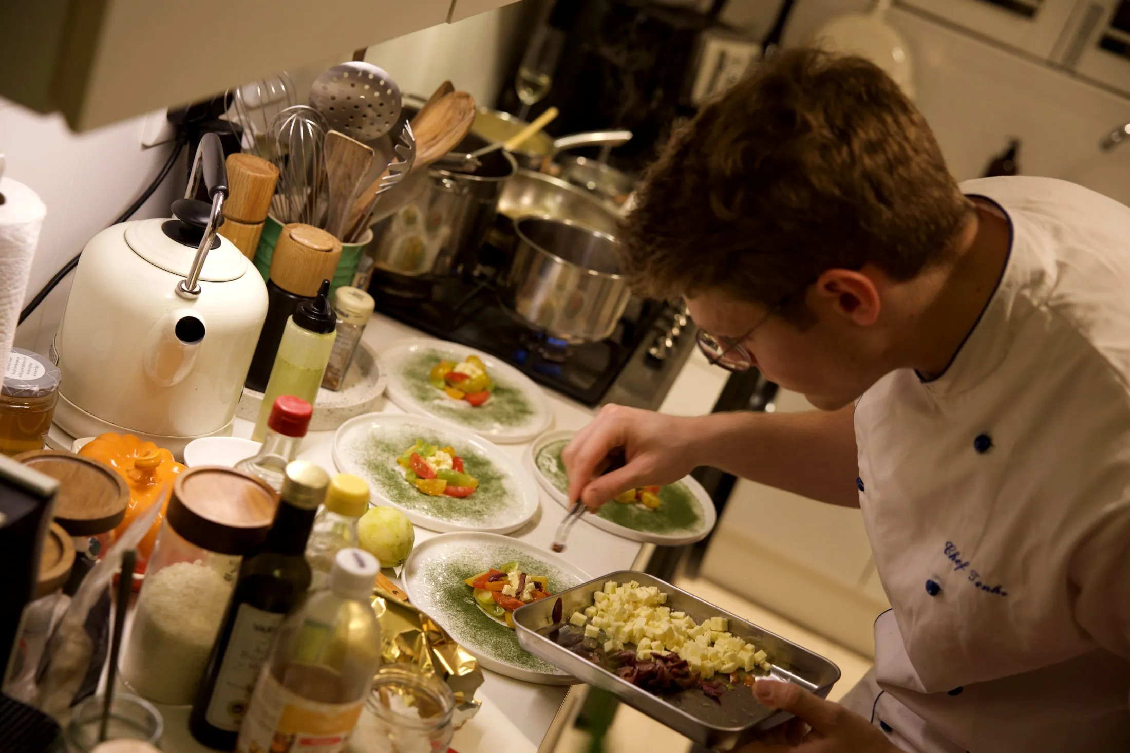 The chef plating dishes at the stove in a domestic kitchen, under warm side light.