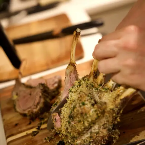 The chef carving a herb-crusted rack of lamb into individual chops.