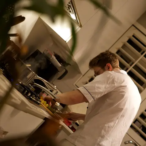 The chef chopping fruit at the stove, steam rising from a pot beside him.