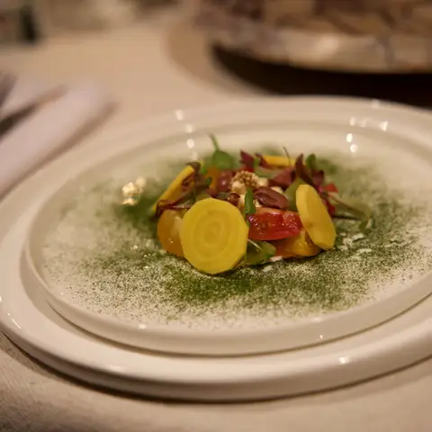 A plated course of golden beet, heirloom tomato and feta with micro herbs, dusted with a herb powder.