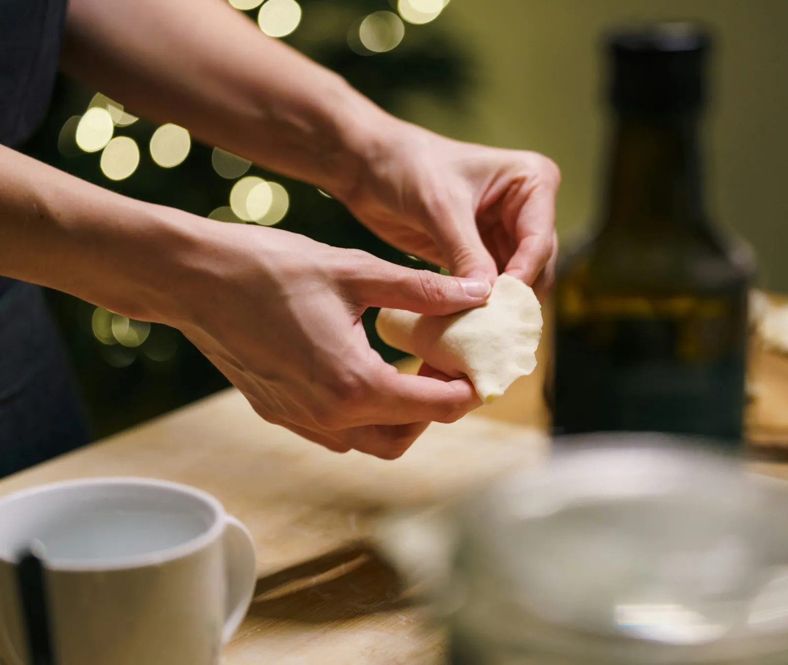 Hands shaping dough on a wooden board in a home kitchen.