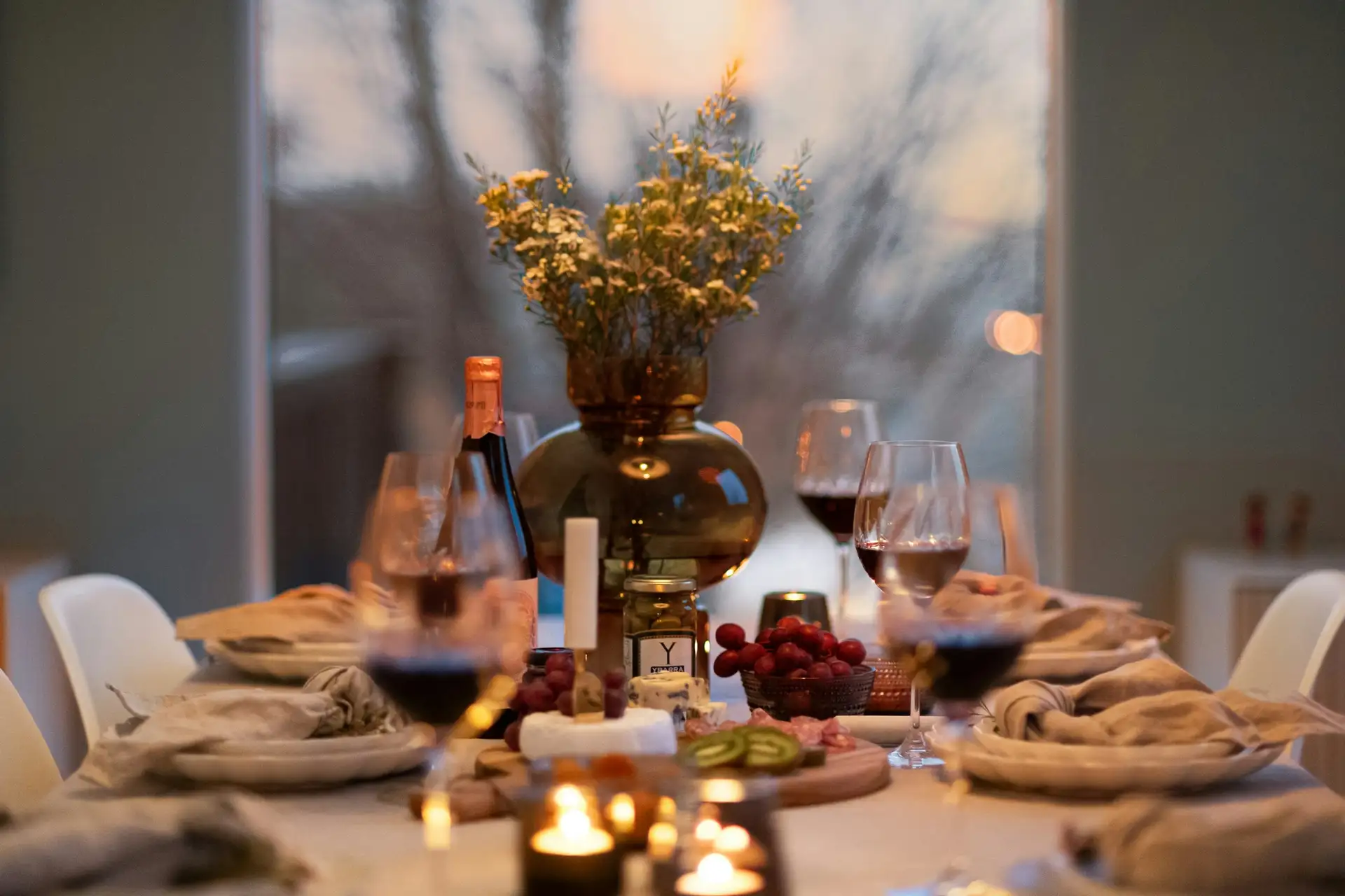 A long table at the end of a dinner, lit by candles, plates and glasses still on the cloth.